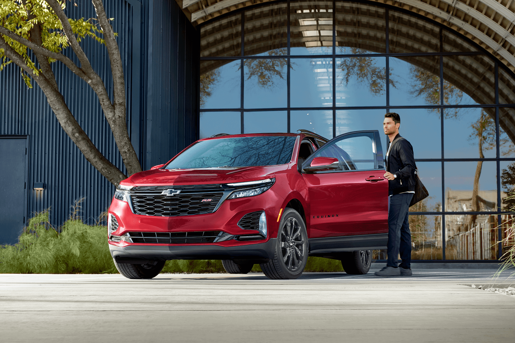 man getting into red chevy equinox in front of luxury home