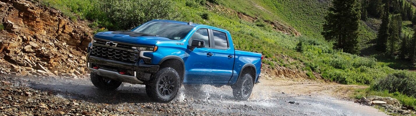 blue chevy truck offroading through large puddle of water